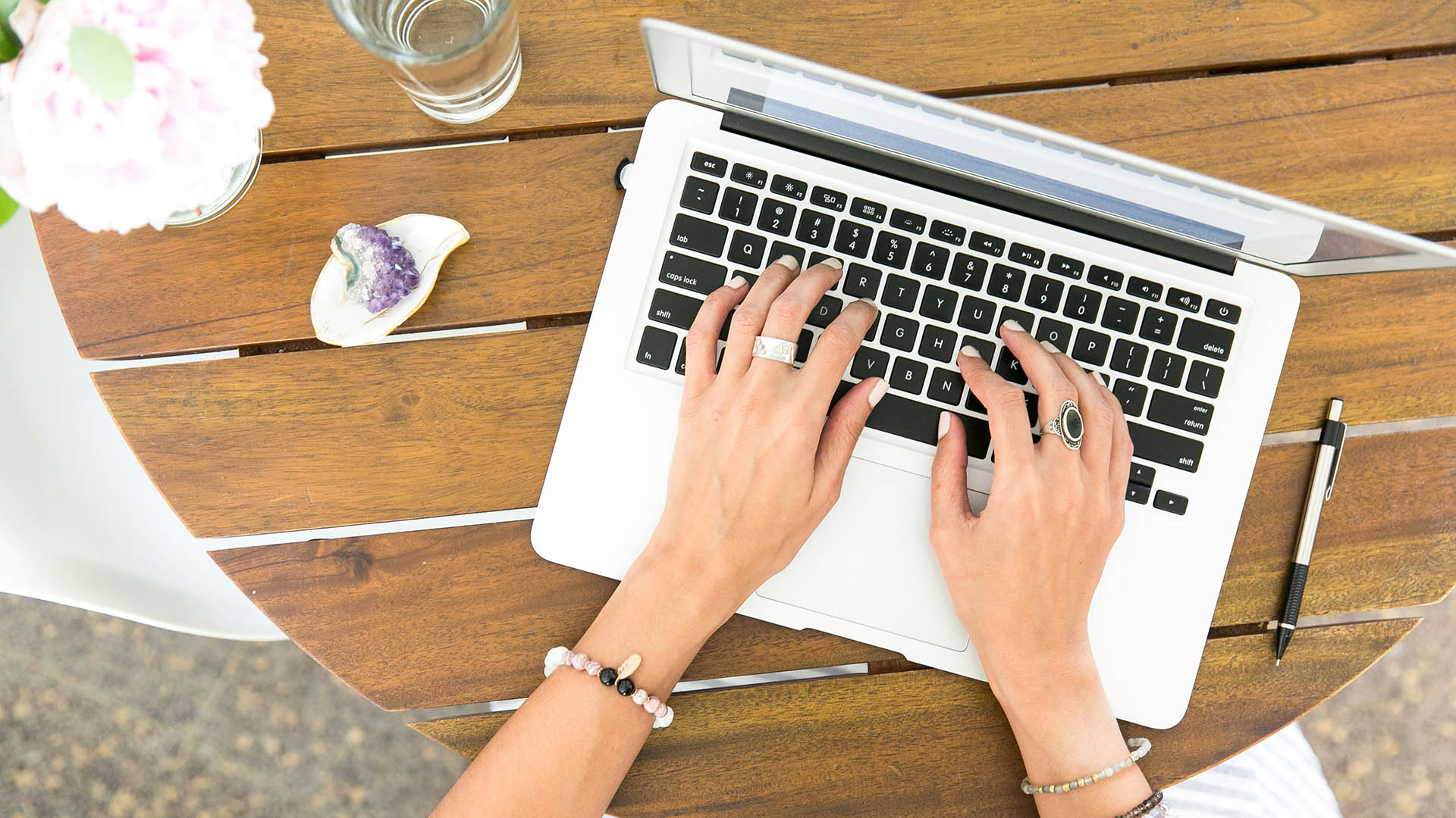 Person working on laptop computer at outdoor table with water glass and sea shell.