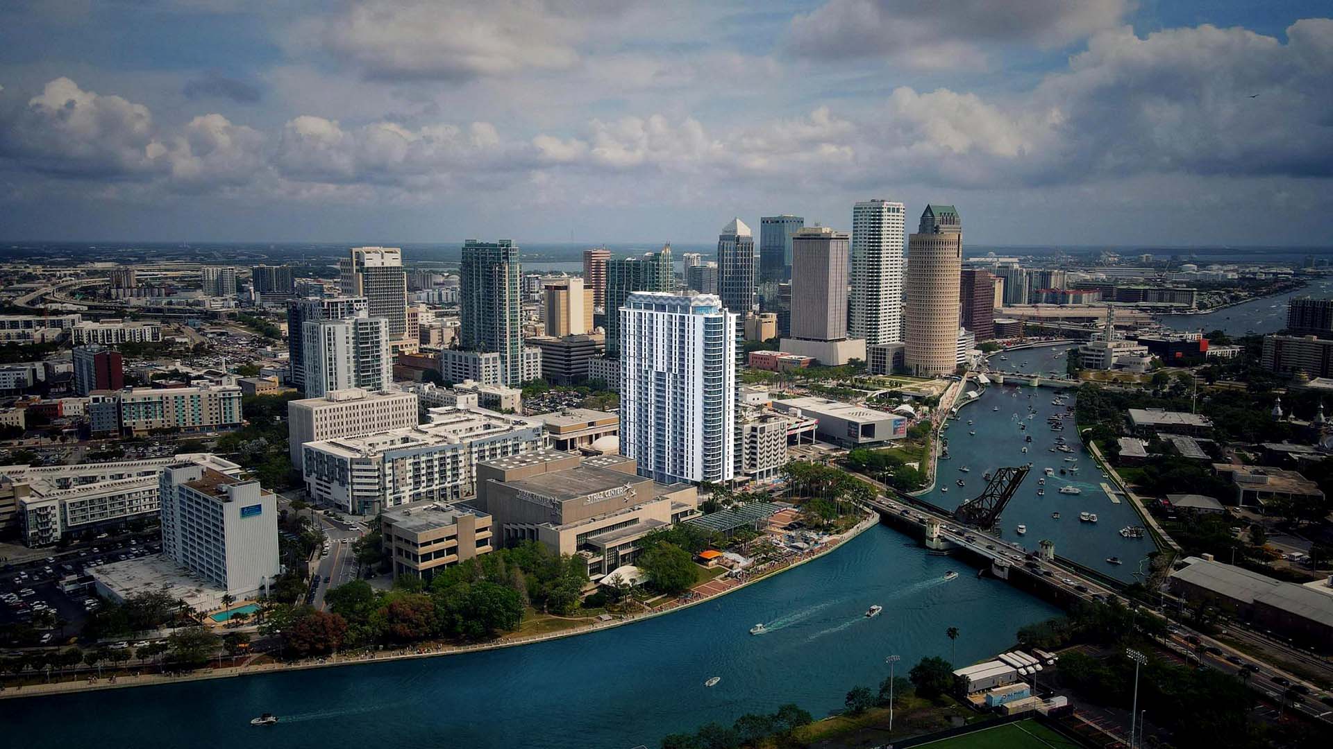 Aerial view of Tampa with towering buildings over bustling waterway.