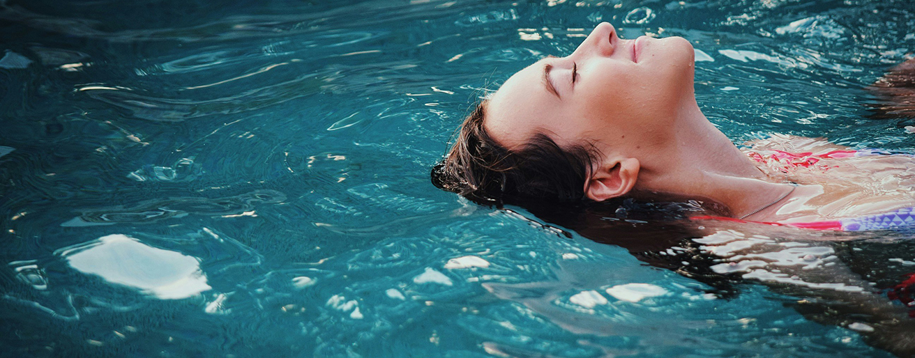 Person relaxing in shimmering swimming pool.